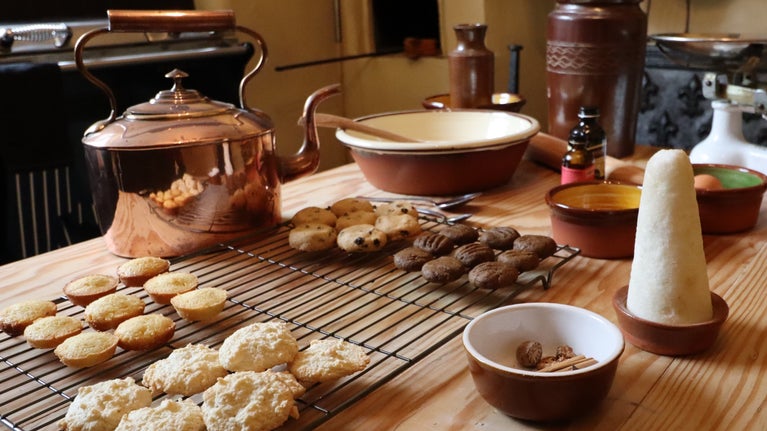 Copper kettle, trays of baked cookies, bowl of cinnamon, pillar of sugar, baking equipment in Quebec House Georgian kitchen